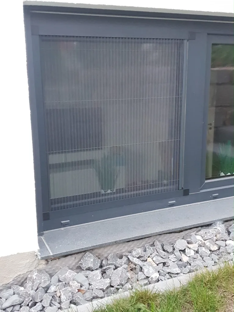 Insektenschutz-Plissee mit anthrazitfarbenem Rahmen an einem bodennahen Fenster