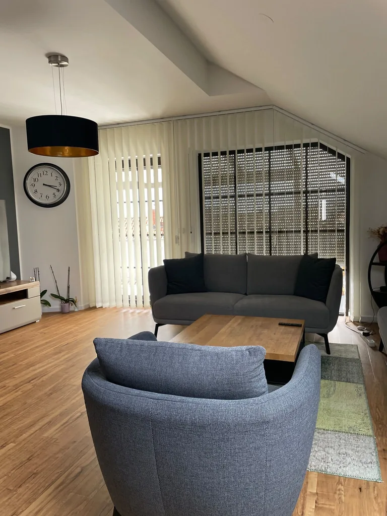 Weiße Vertikallamellen an einer Fensterfront unter der Dachschräge im Wohnzimmer