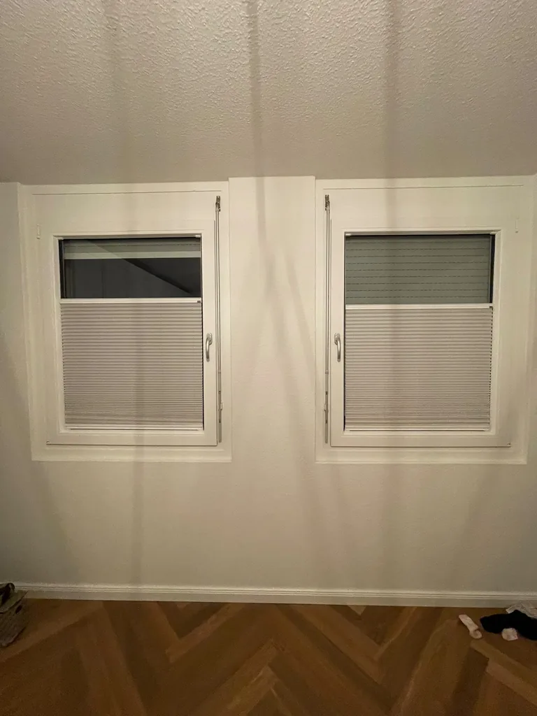 Beige Plissees als Sichtschutz im unteren Bereich zweier weißer Fenster