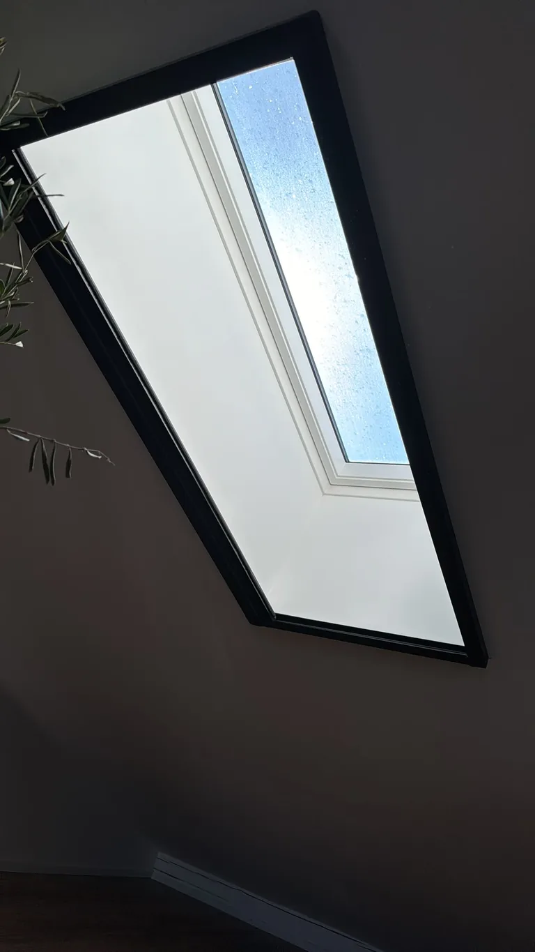 Vollständig geöffnetes Faltplissee im schwarzen Rahmen vor einem Dachfenster